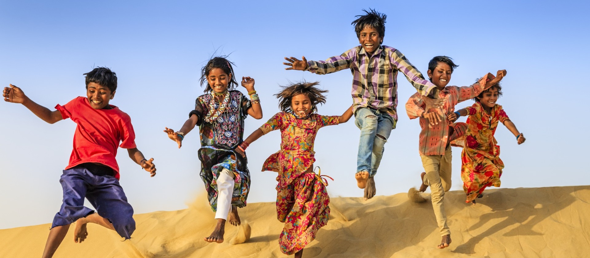 Children running and jumping on a sand dune