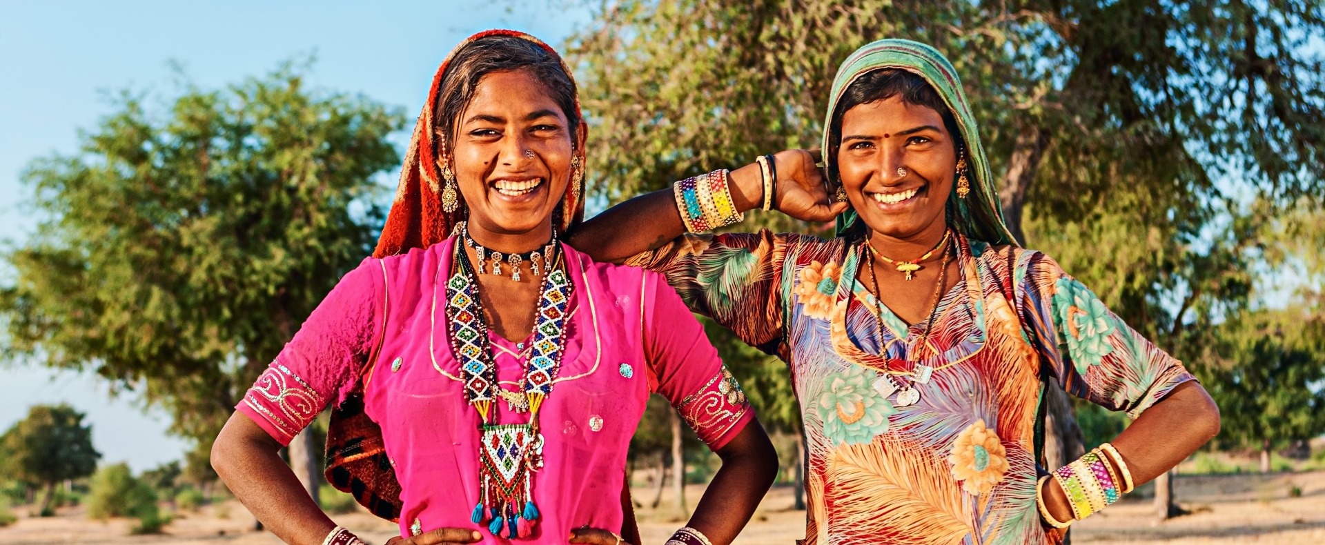 Two Indian women smiling at the camera with colorful dresses